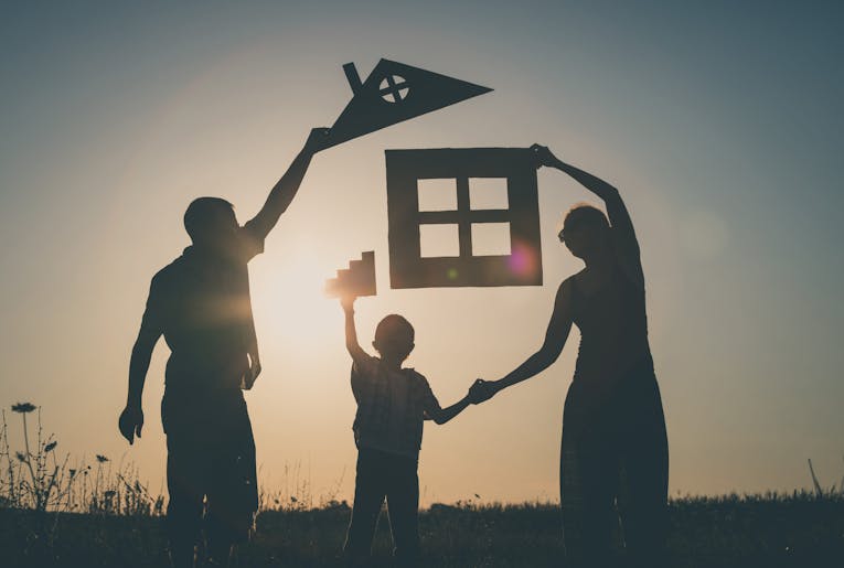 Happy family standing on the field at the sunset time. They build a house. Concept of friendly family.