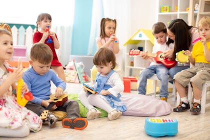 Kindergarten teacher with children on music lesson in day care. Little kids toddlers play together with developmental toys.